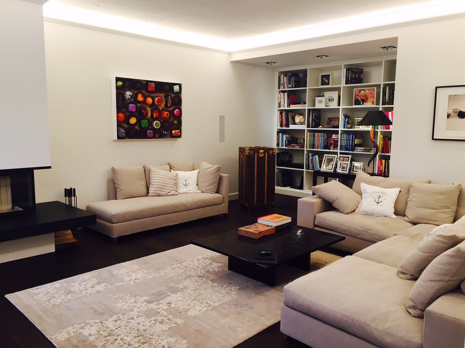 Modernes Wohnzimmer: zwei beige Sofas, schwarzer Couchtisch, großes Bücherregal und Teppich.