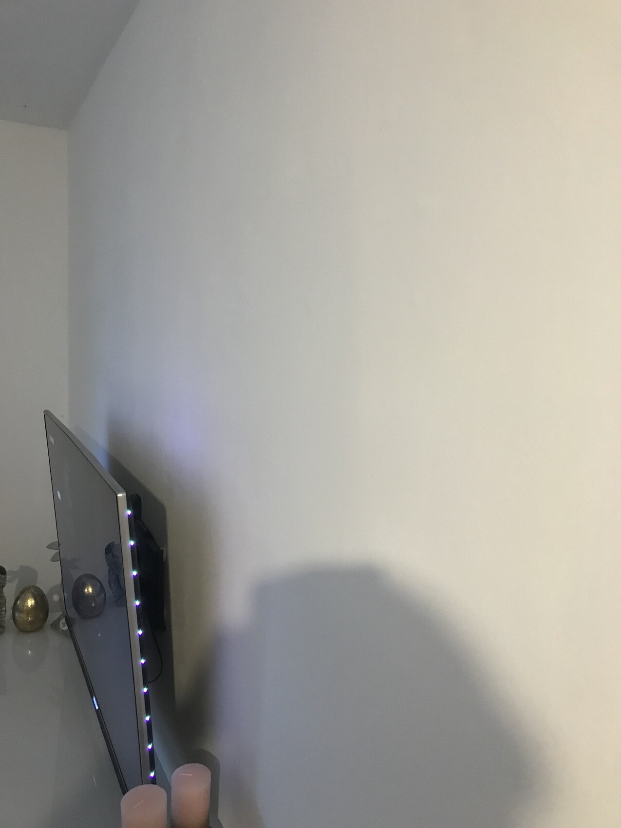 Flachbildschirm an der linken Wand mit LED-Lichtleiste, darunter Kerzen und Deko.
