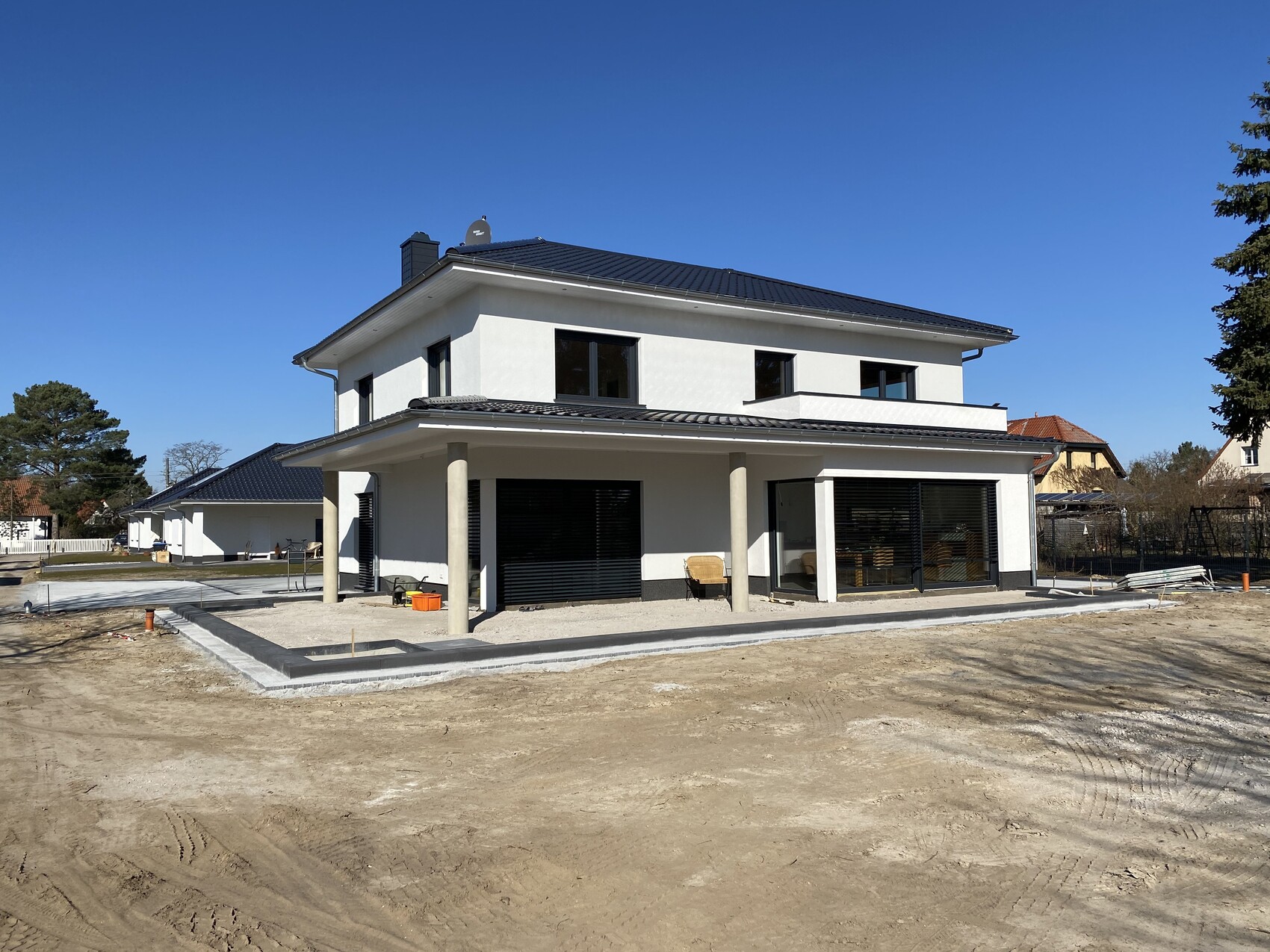 Modernes weißes Einfamilienhaus mit überdachter Terrasse, Bauplatz davor.