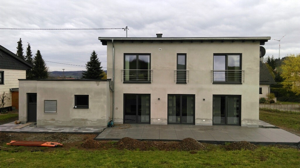 Modernes zweistöckiges Haus mit Glas-Schiebetüren, Balkonen und Terrasse, Baufläche.
