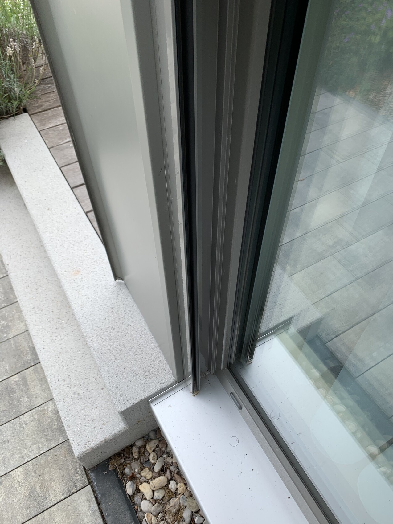 Nahaufnahme eines Glas-Schiebetürrahmens am Boden, Außenbereich mit Kieselsteinen.