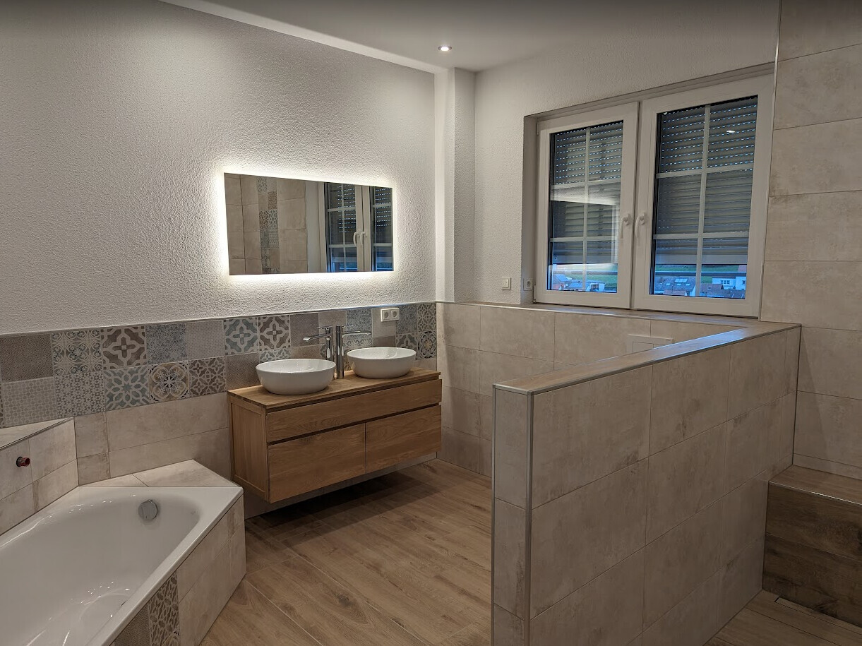 Modernes Badezimmer mit Badewanne, Doppelwaschbecken, Holzunterschrank und beleuchtetem Spiegel.