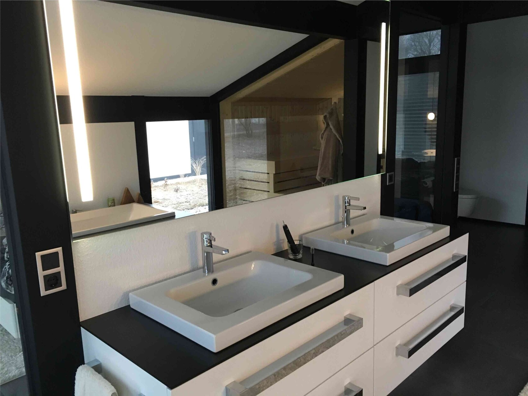 Modernes Badezimmer mit Doppelwaschtisch, zwei Waschbecken, schwarzer Unterbau und Spiegelwand.