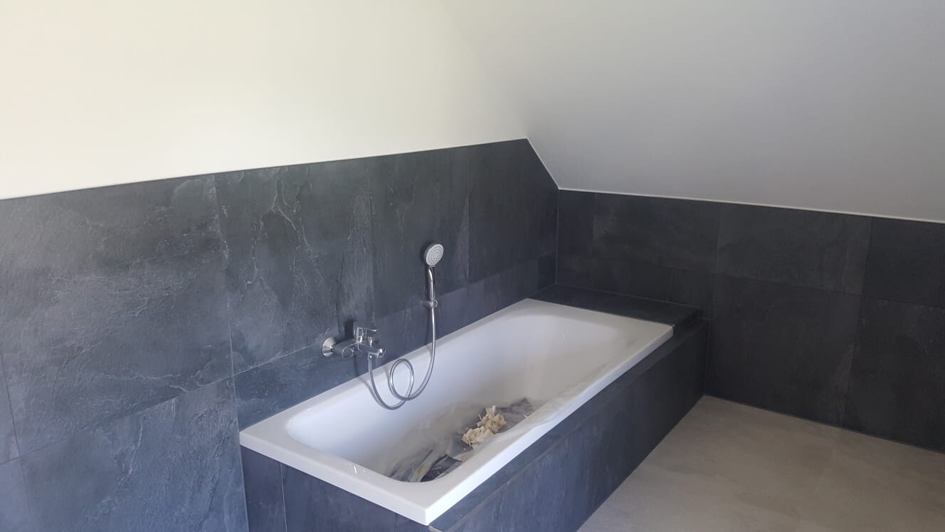 Dunkle Fliesen um eine eingelassene rechteckige Badewanne mit Handbrause im modernen Bad.