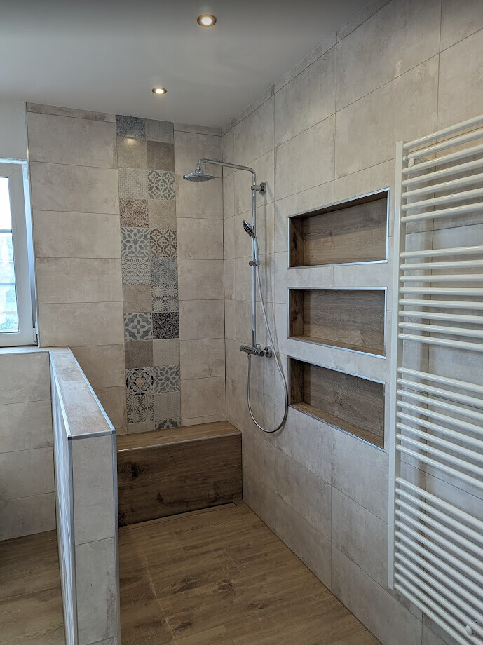 Modernes Bad mit beigen Fliesen, Dusche, Holzbank und Handtuchheizkörper.