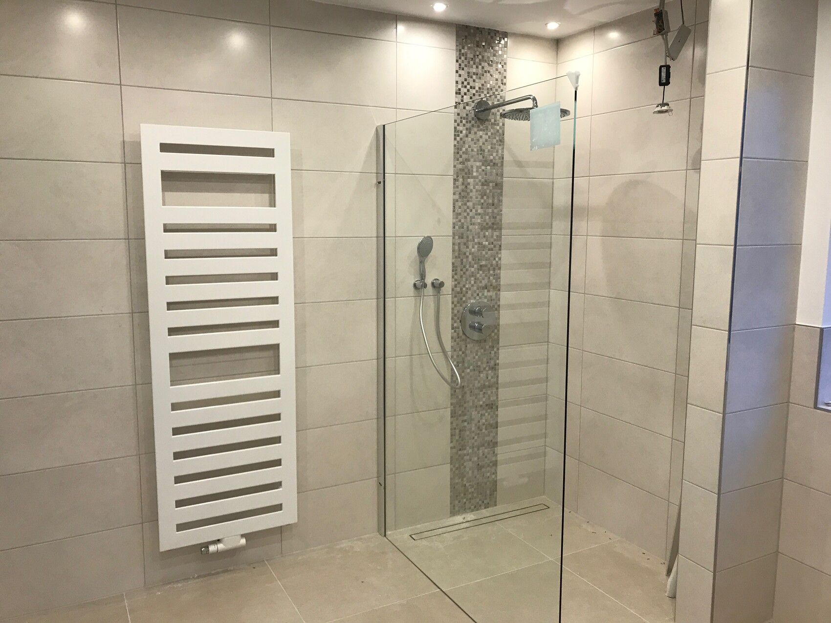 Modernes Badezimmer mit Glas-Dusche, Mosaikstreifen an der Wand und weißem Handtuchheizkörper.