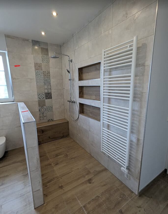 Modernes Badezimmer mit Dusche, Holzbank, Nischenregalen, Heizkörper und Fenster links.