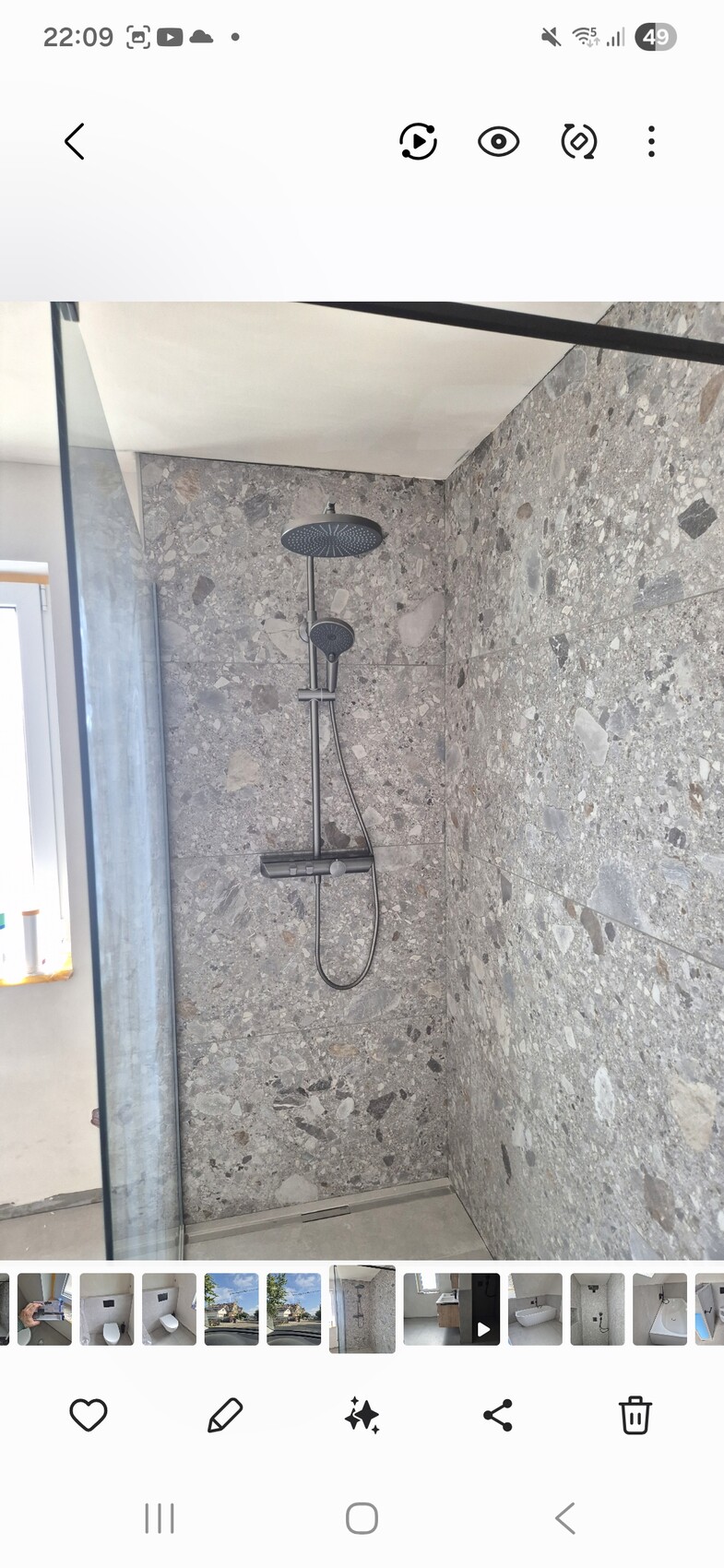Duschbad mit großer Regendusche und Handbrause vor Steinfliesen.