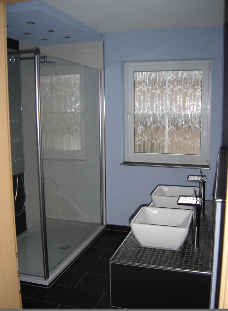 Badezimmer mit Dusche und zwei Waschbecken auf dunklem Waschtisch, blaue Wände.
