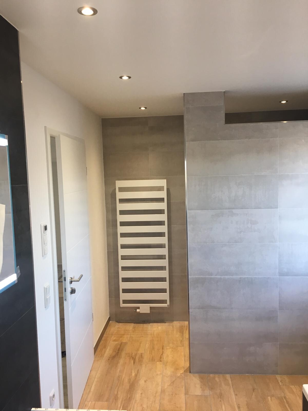 Modernes Badezimmer mit weißer Handtuchheizung an grauer Wand und Holzboden.