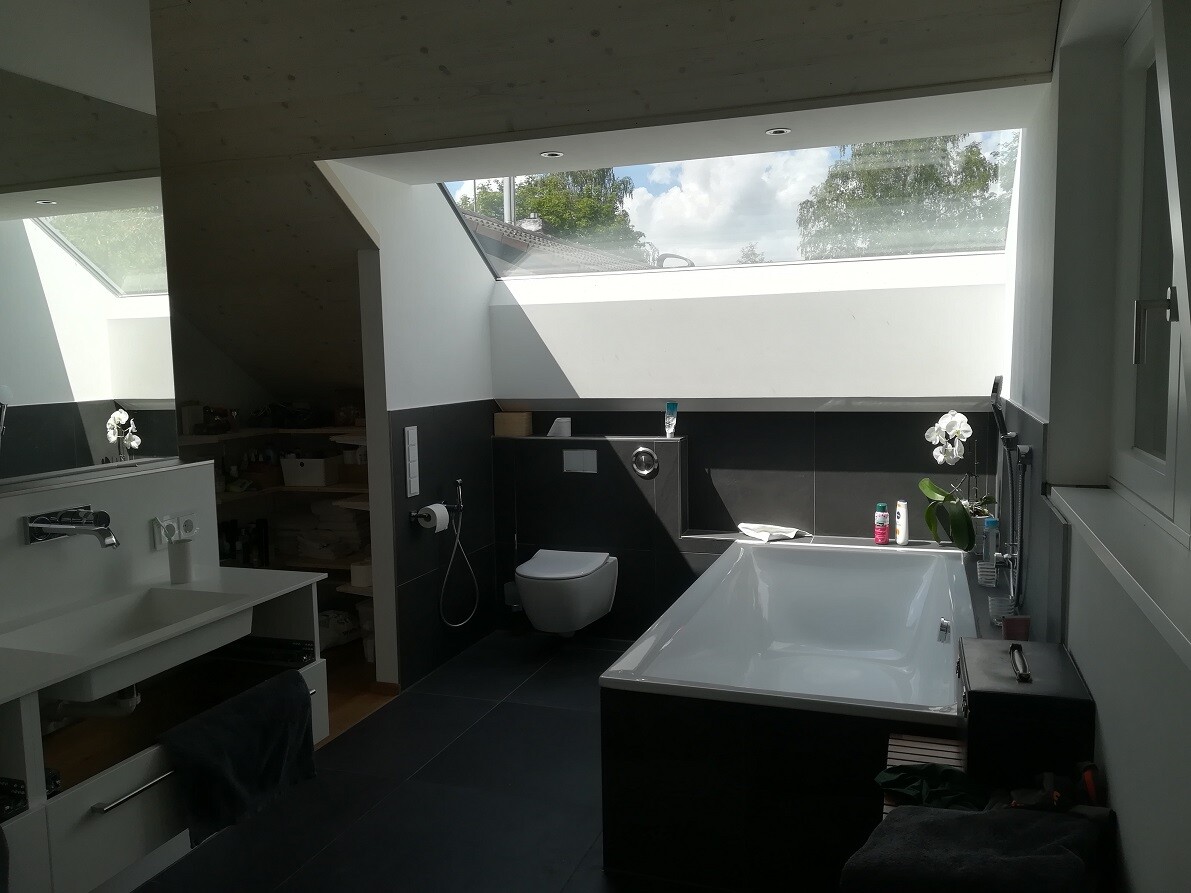 Moderneres Badezimmer mit großer Badewanne unter Dachfenster, Waschbecken links, Toilette in Mitte.
