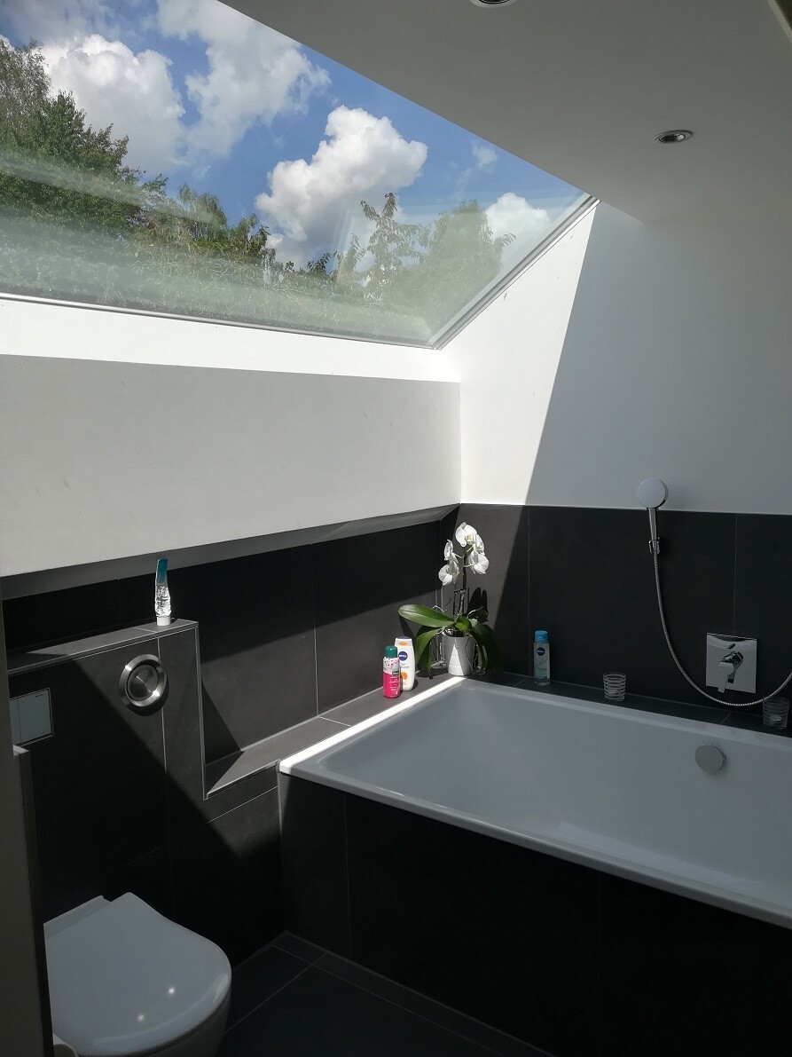Moderner Badraum mit großem Dachfenster, Badewanne, dunklen Fliesen und Orchidee.