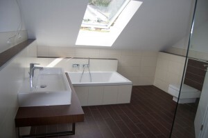 Helles modernes Badezimmer mit Badewanne, Waschtisch und Glasdusche unter Dachfenster.