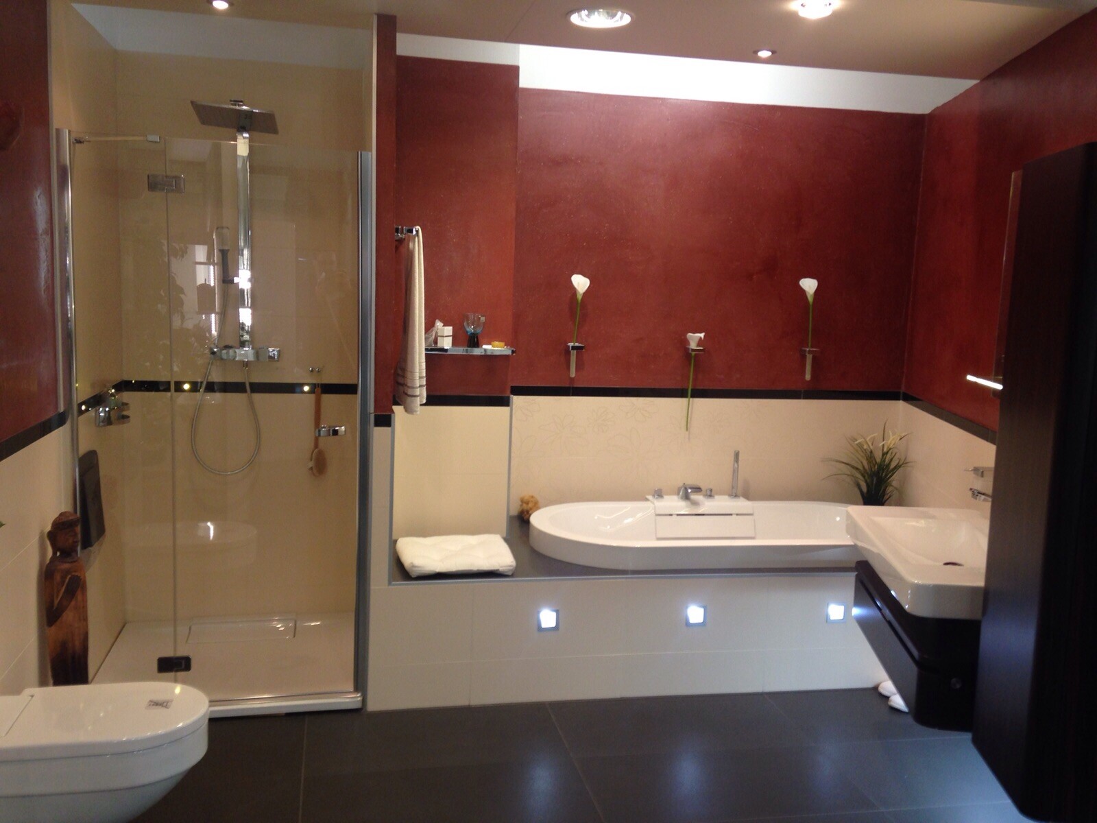 Modernes Badezimmer mit Glasdusche links, Badewanne an der Rückwand und weiße Calla-Lilien.