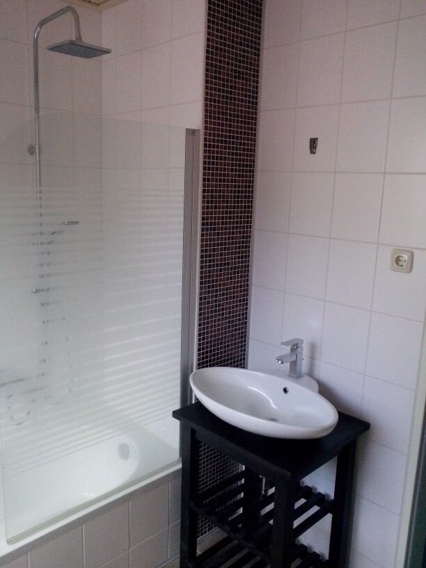 Modernes Bad: Dusche hinter Glasabtrennung, rundes weißes Waschbecken auf schwarzem Unterbau.