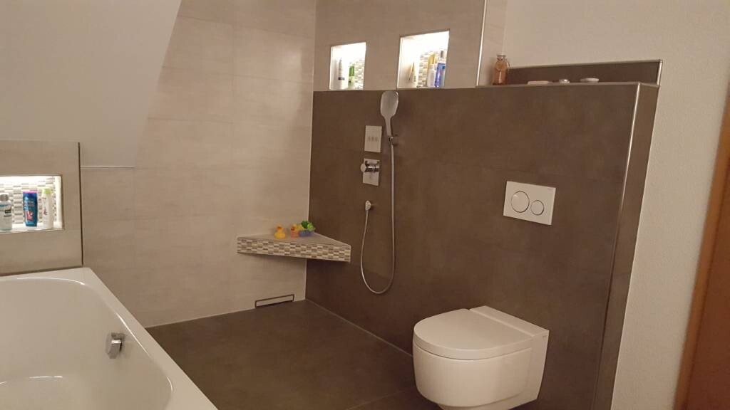 Modernes Badezimmer mit Badewanne links, Dusche an dunkler Wand, Toilette rechts.