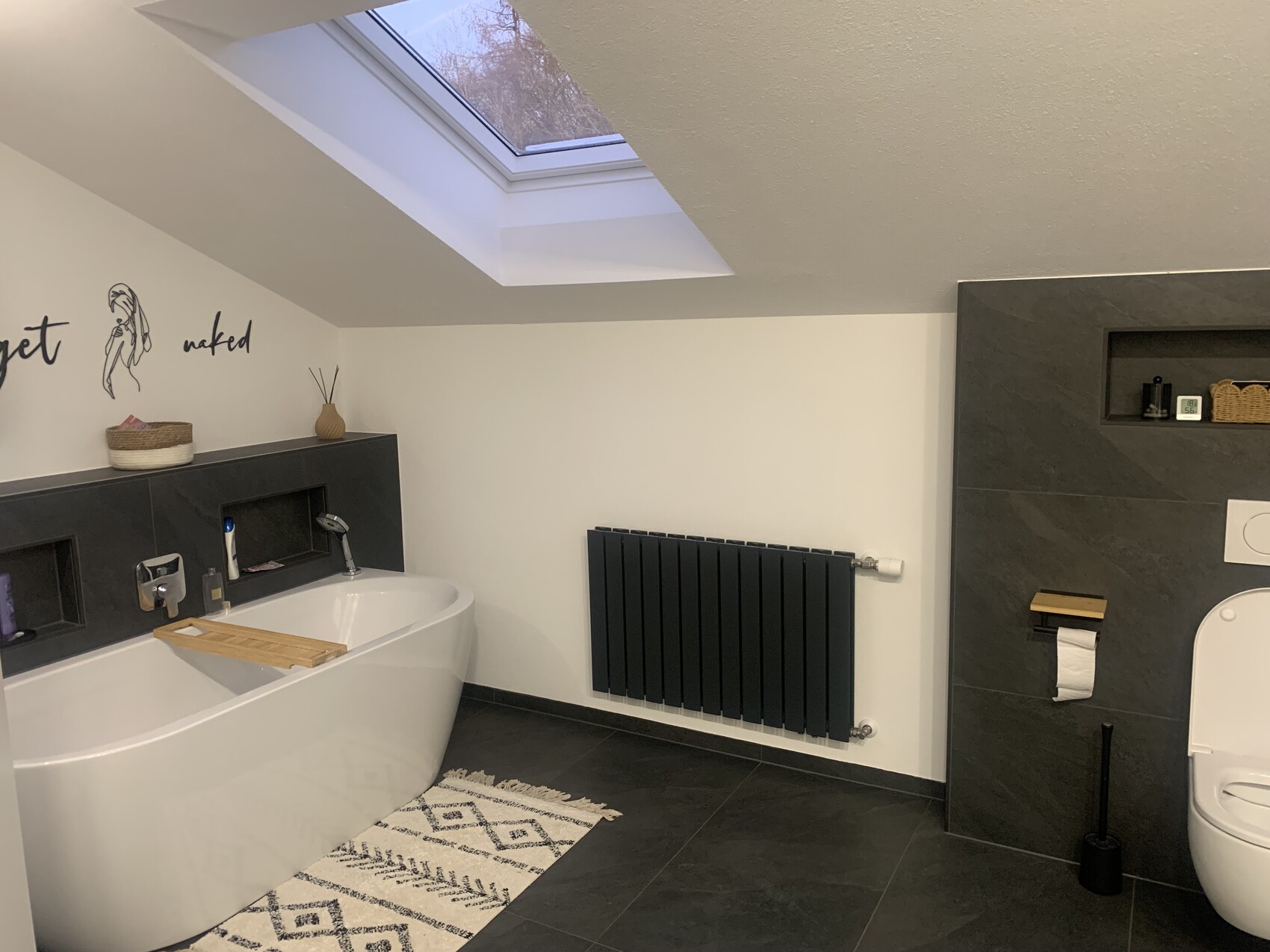 Modernes Badezimmer mit freistehender Badewanne, Dachfenster und dunklen Fliesen.