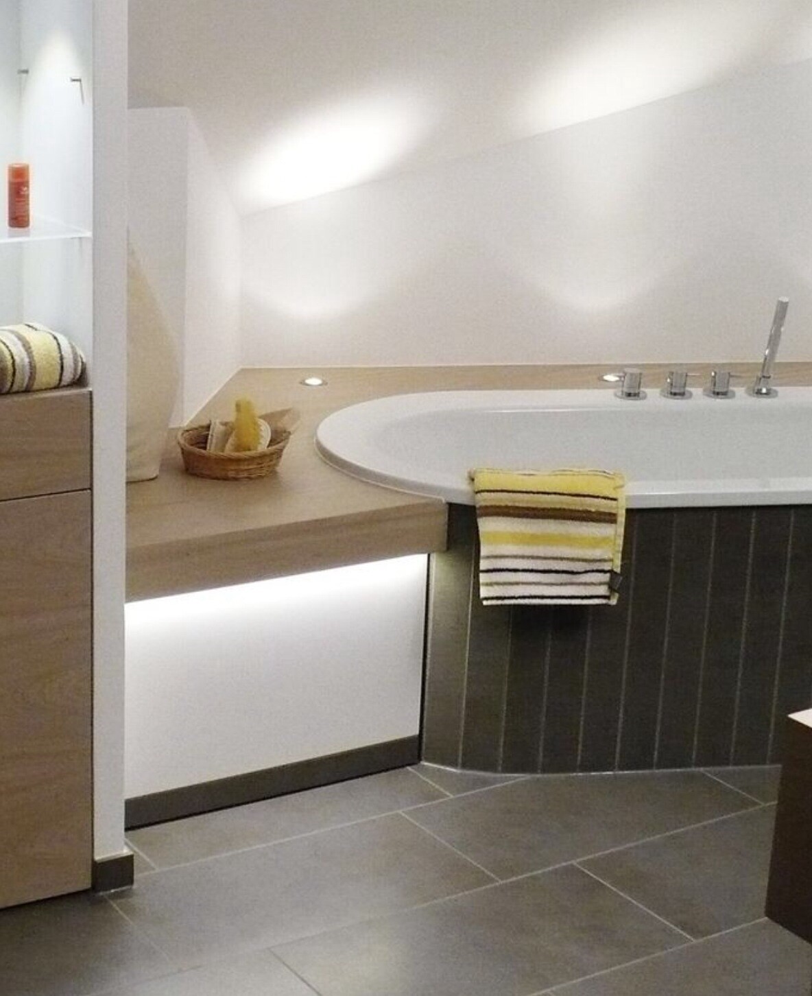Modernes Badezimmer mit integrierter Badewanne, gelb gestreiftem Handtuch und Körbchen auf der Ablage.