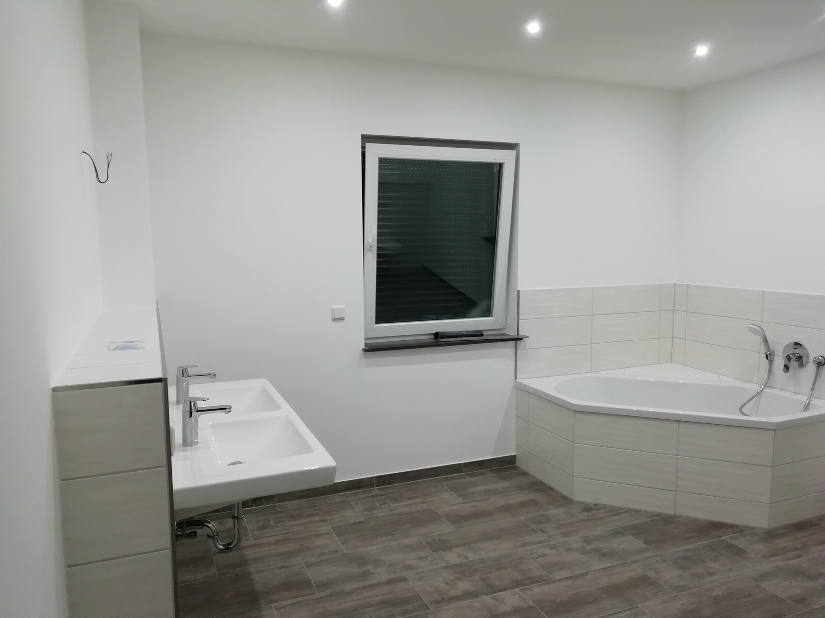 Modernes Badezimmer mit Eckbadewanne, Doppelwaschbecken, Fenster und grauen Bodenfliesen.