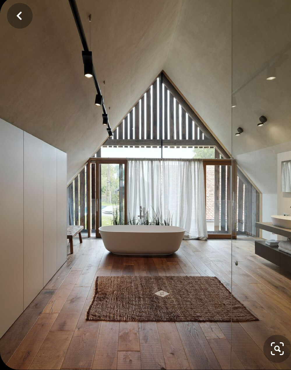 Freistehende Badewanne in Loft-Badezimmer mit Holzboden, Glaswänden und Vorhängen