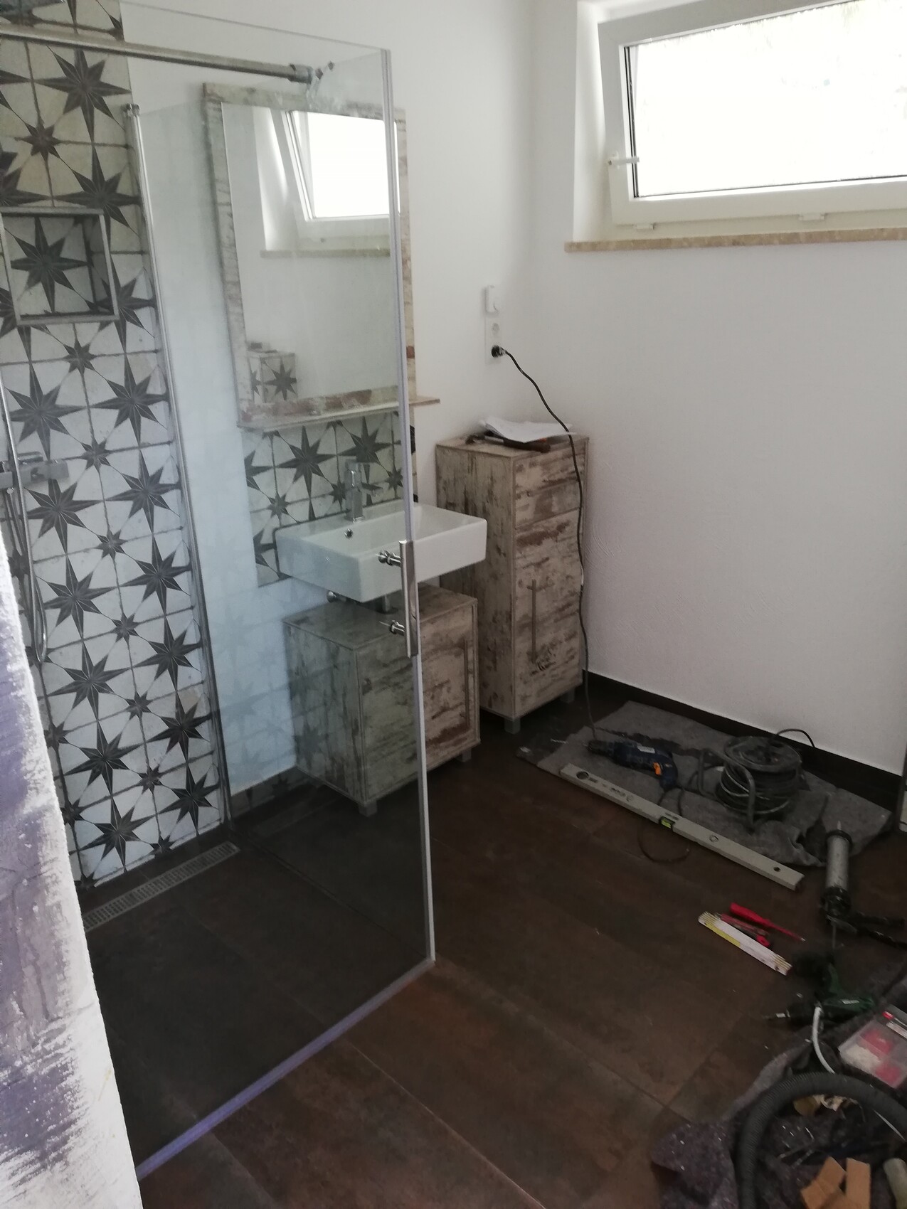 Badezimmer Renovierung: Glasdusche links, Waschbecken, Sternmuster-Fliesen, Werkzeuge auf dem Boden.