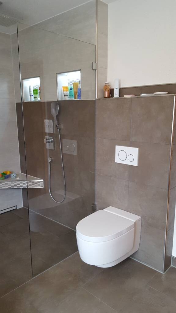 Modernes Badezimmer mit Glasdusche, wandhängendem WC und grauen Fliesen.