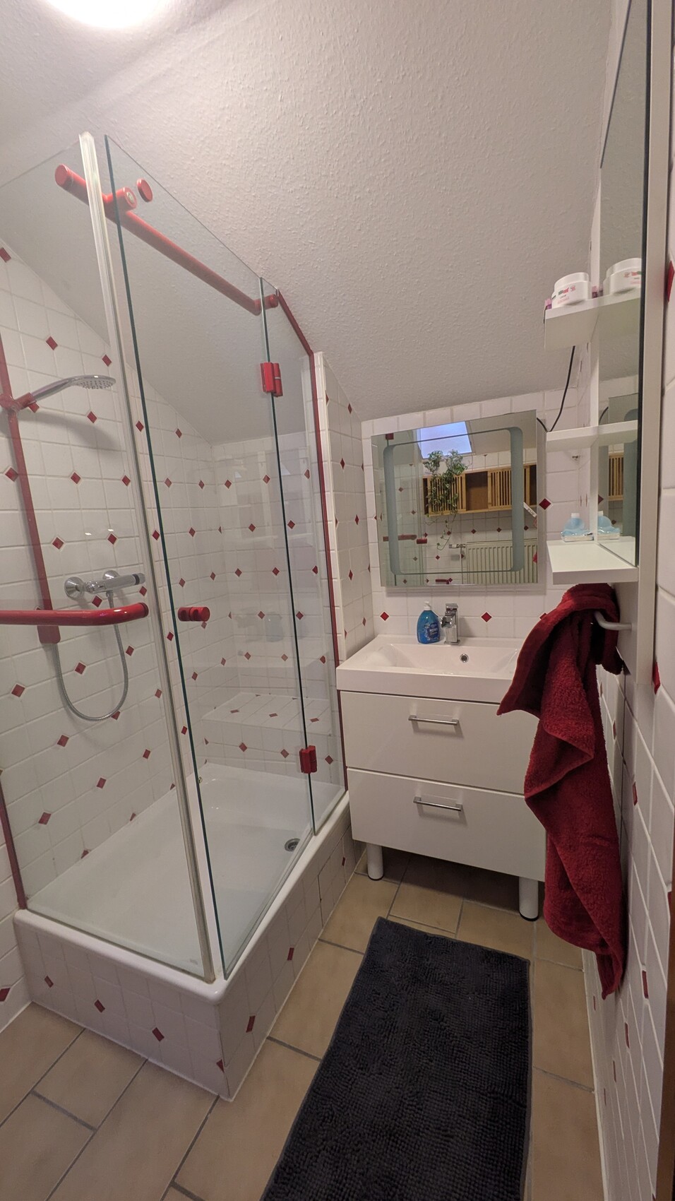 Kleines Badezimmer mit Glasdusche, weißem Waschbeckenunterschrank und rotem Handtuch.