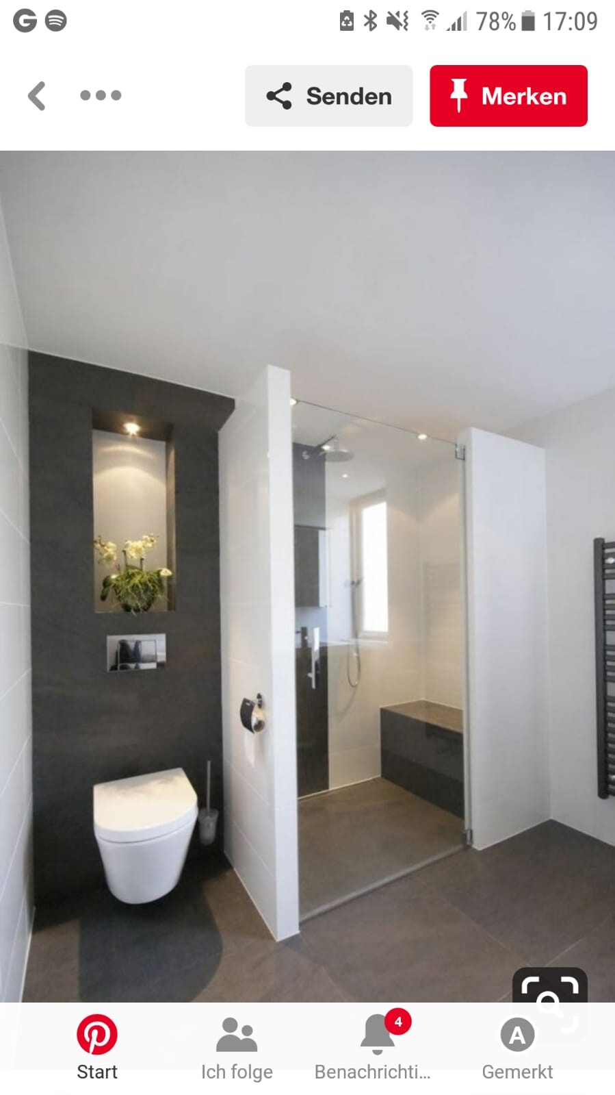 Modernes Badezimmer mit wandhängendem WC, Glasduschkabine, dunkler Nischenwand mit Pflanze und Sitzbank.