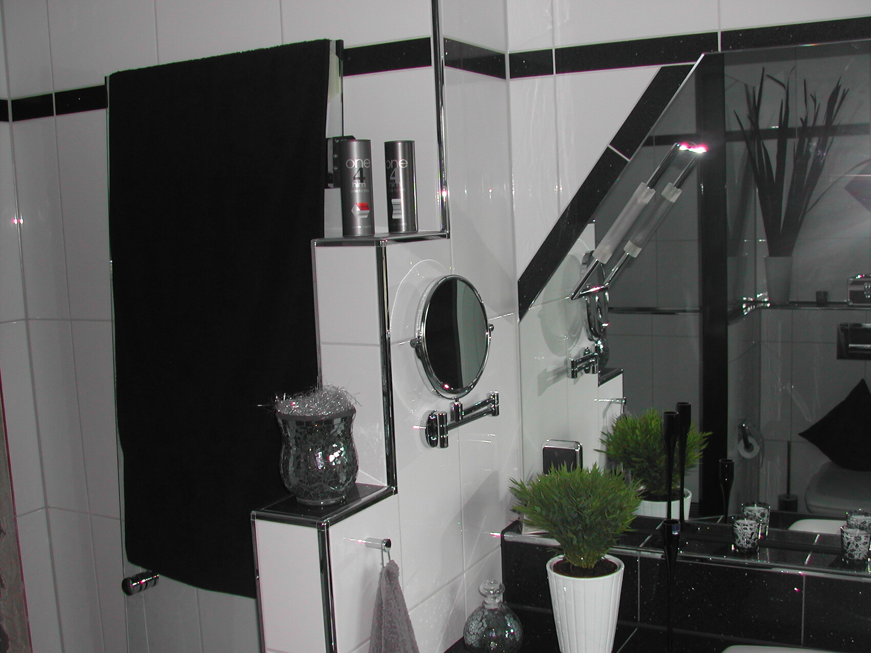 Modernes Badezimmer mit Spiegel, Rundspiegel, Pflanze in weißem Topf und Schwarz-Weiß-Fliesen.