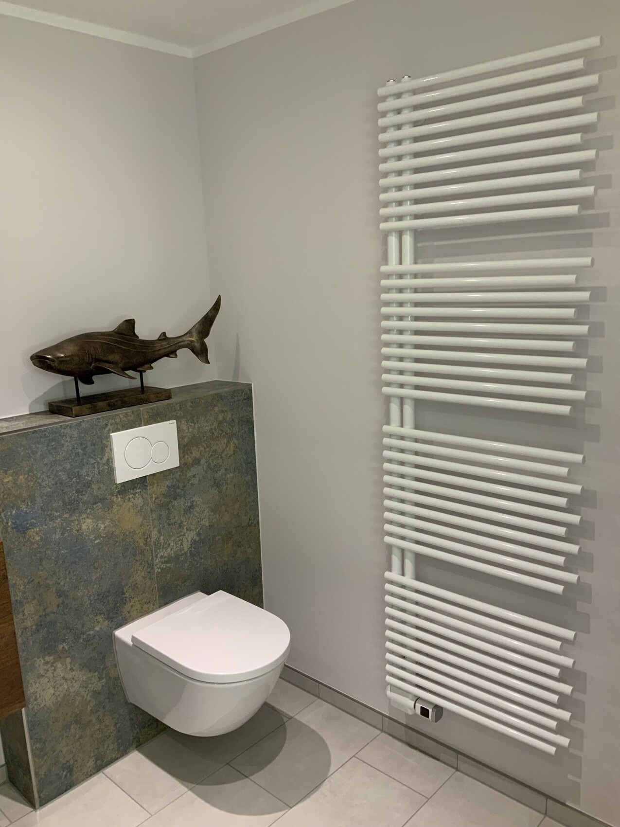 Modernes Bad: wandhängendes WC, Steinplatte, Haifisch-Skulptur, weißer Heizkörper.