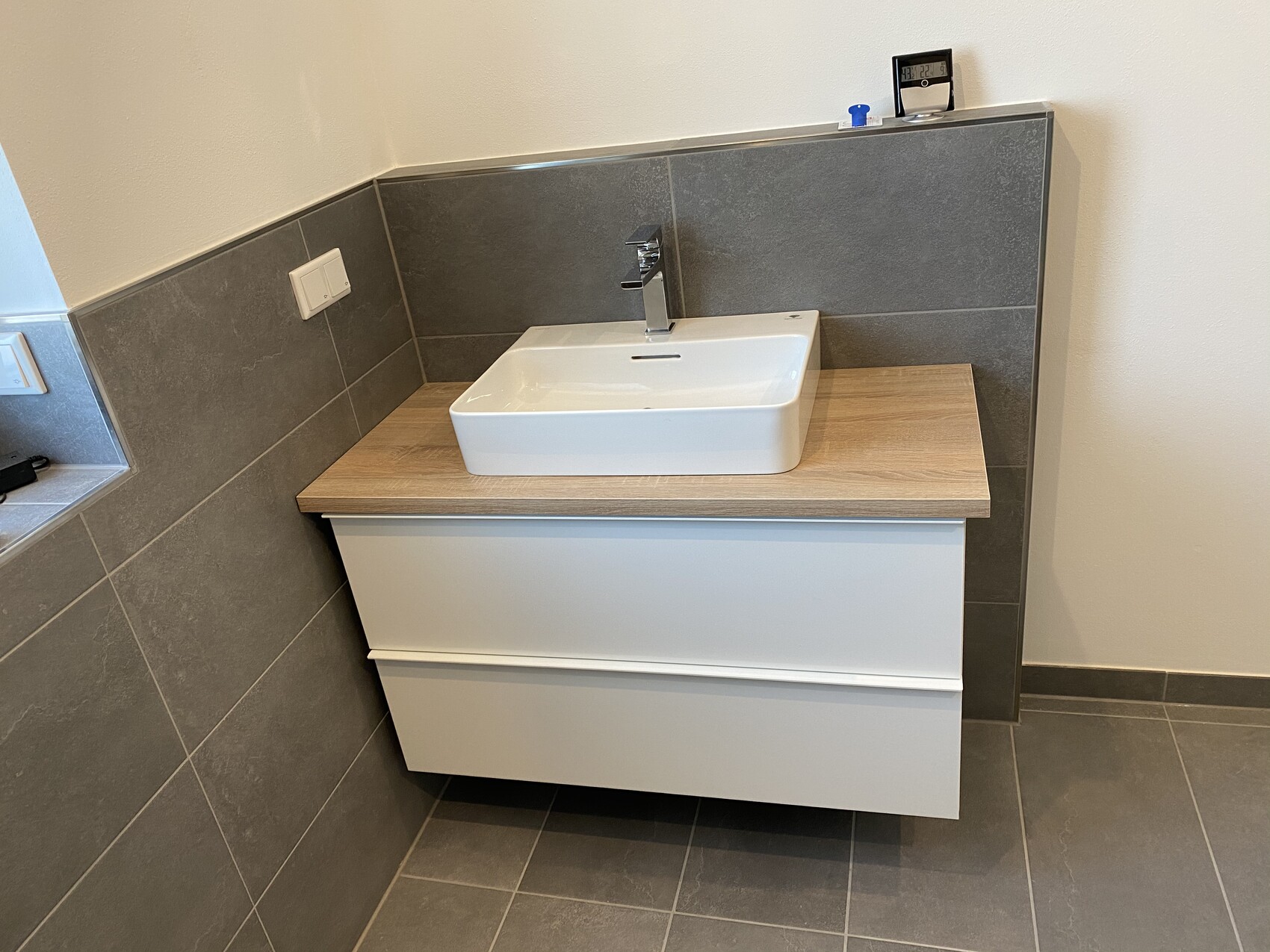 Moderne Badezimmer-Waschtisch mit rechteckigem weißen Becken auf Holzplatte, grauen Fliesen.