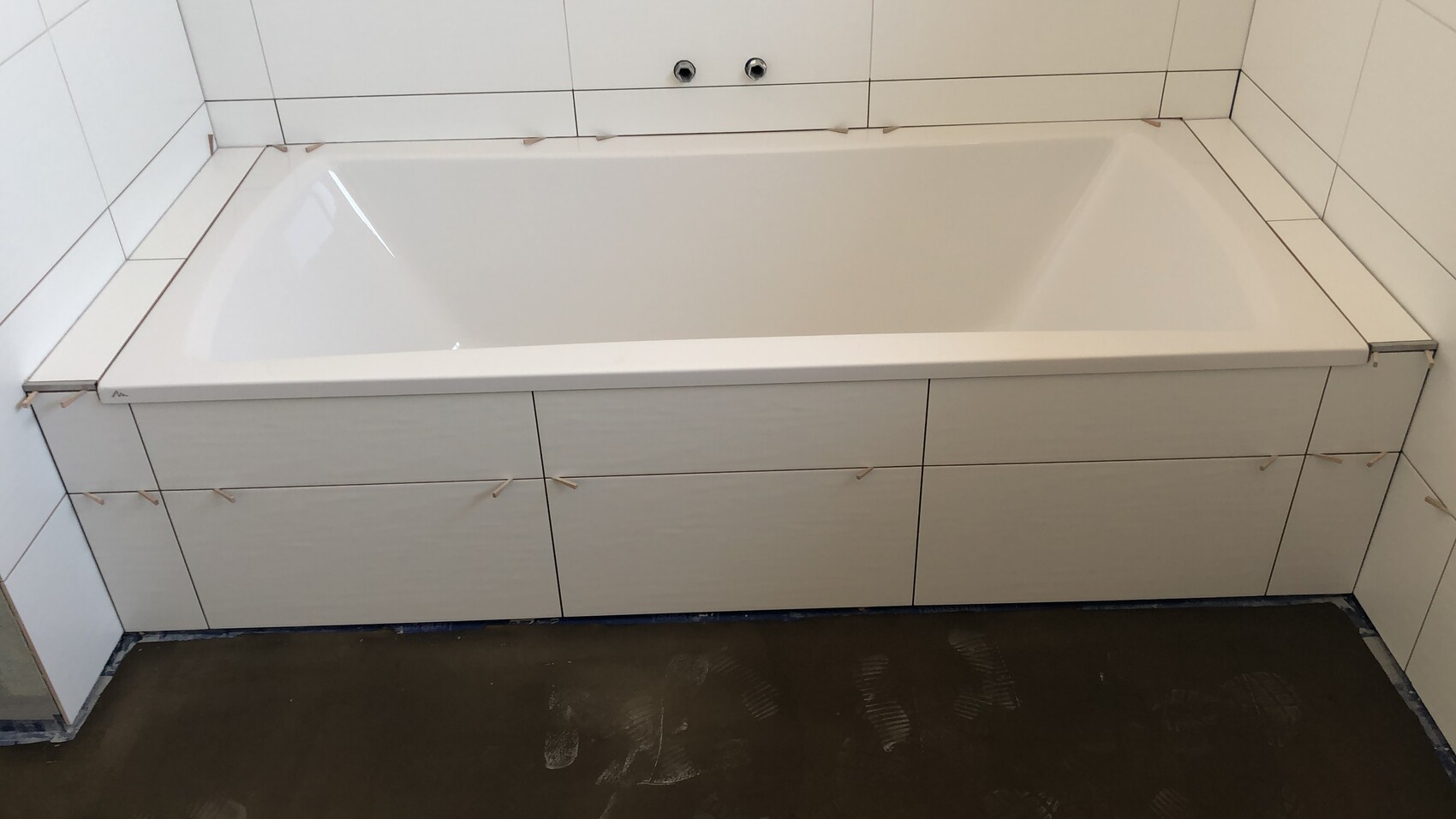 Weiße Badewanne mit Unterschrankfronten, Fliesenwand, Armaturen fehlen – Baustellenstatus