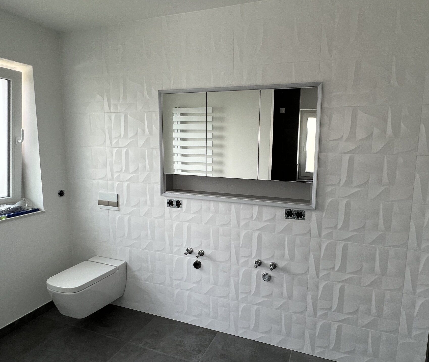 Modernes Badezimmer mit wandhängendem WC, 3D-Fliesen, großem Spiegel mit Ablage, Fenster links.