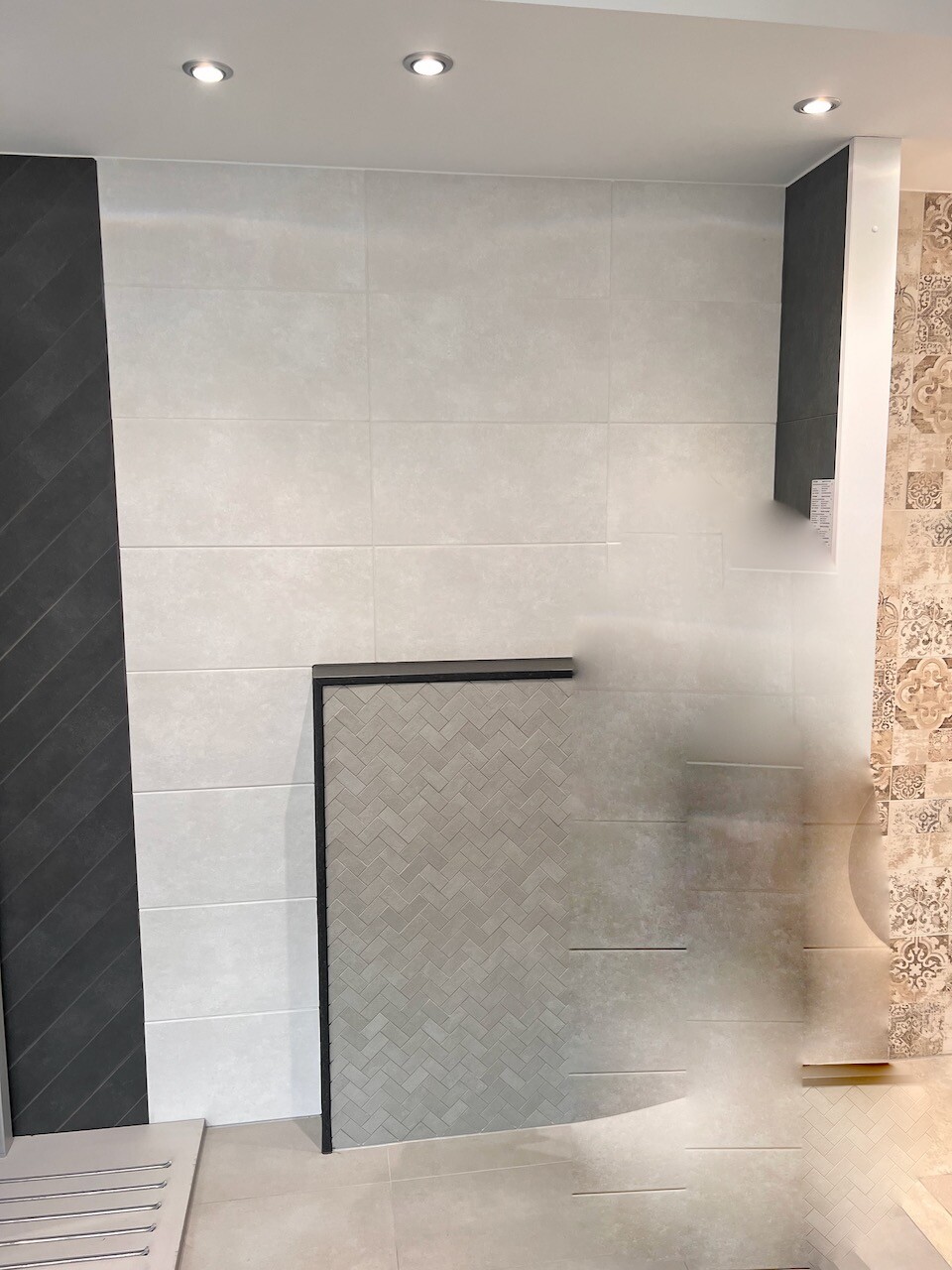 Badezimmer-Showroom mit hellgrauen Fliesen, schwarzem Rahmen, Nischen-Dusche mit Zickzack-Muster.