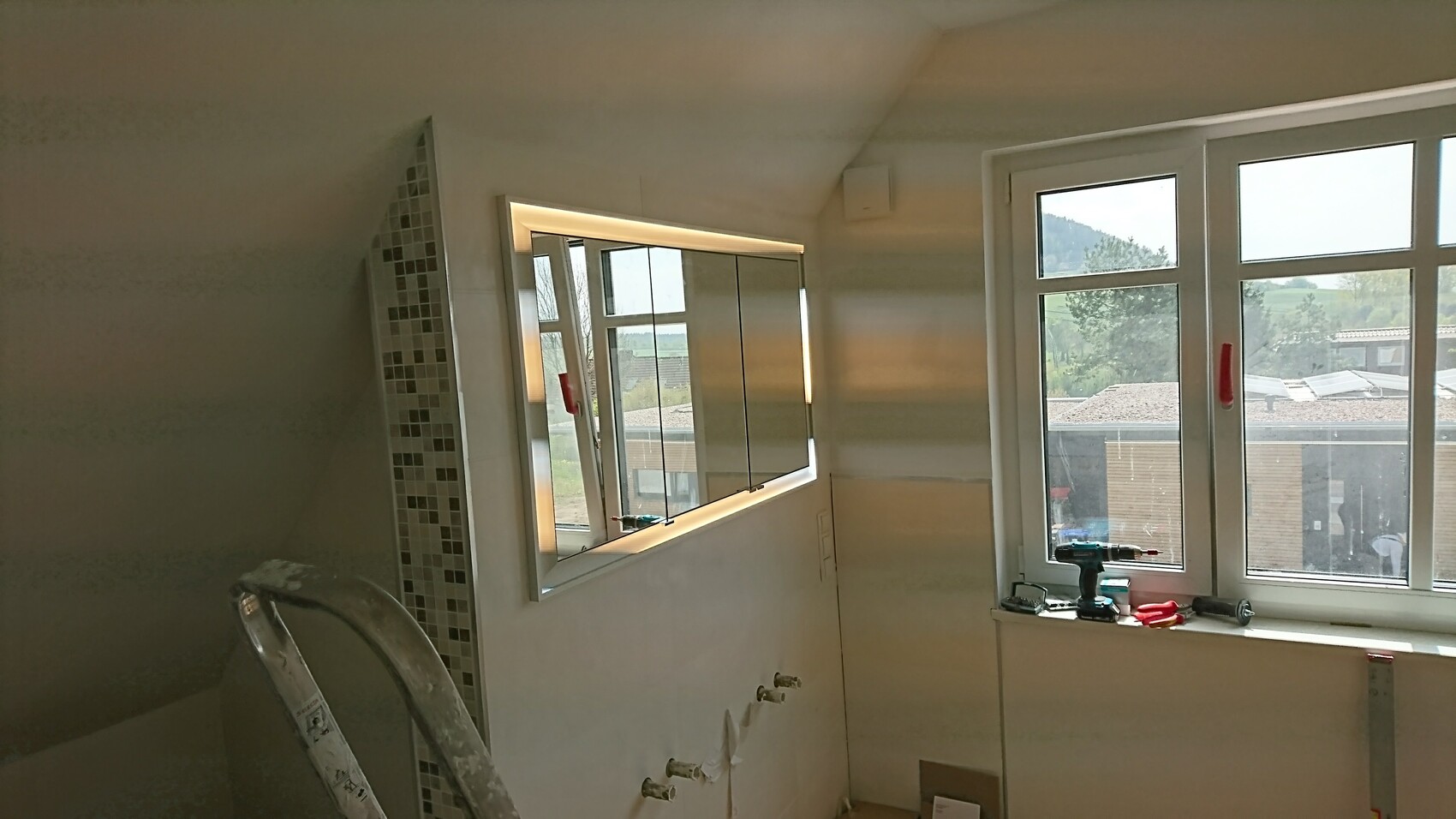 Modernes Badezimmer im Renovierungszustand mit beleuchtetem Spiegelschrank, Werkzeugen und Leiter.