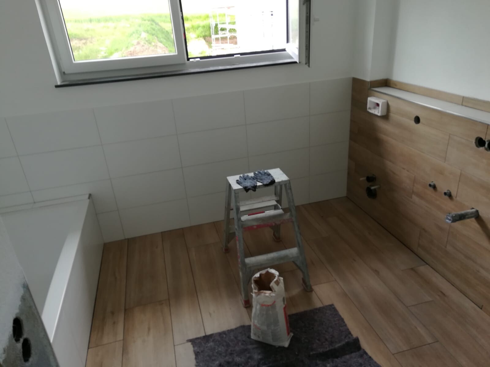 Badezimmer im Umbau: Fenster, weiße Fliesen links, Holzoptik-Wand rechts, Leiter in der Mitte.
