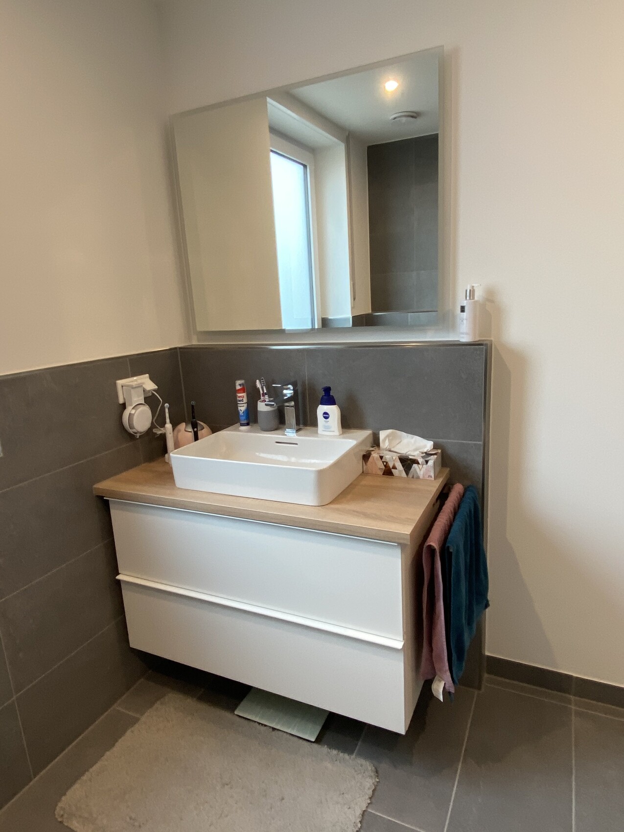 Moderne Badezimmer-Waschtisch-Kombination mit rechteckiger Spüle, Spiegel und Handtüchern.
