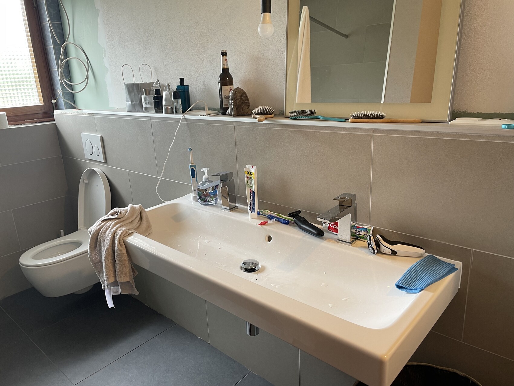 Waschbecken im Badezimmer mit Spiegel, Zahnpasta, Zahnbürsten, Rasierer, WC.