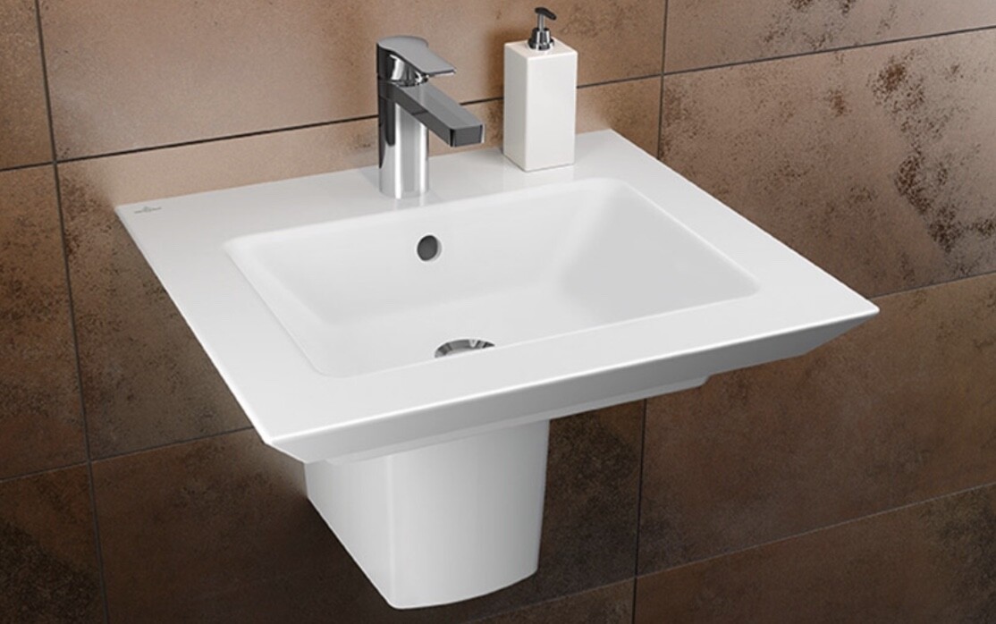 Weißes wandhängendes Waschbecken mit Chromarmatur und Seifenspender vor braunen Fliesen.