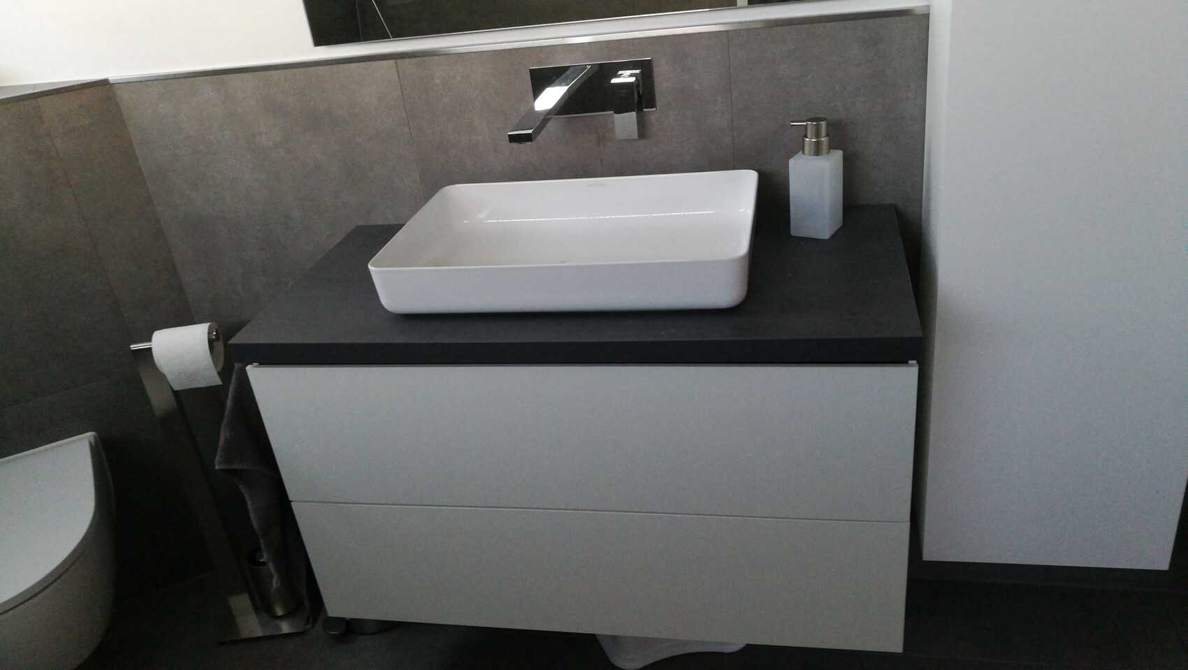 Moderner Bad-Waschtisch: rechteckige Spüle, Wandarmatur, Seifenspender und Toilettenpapier.