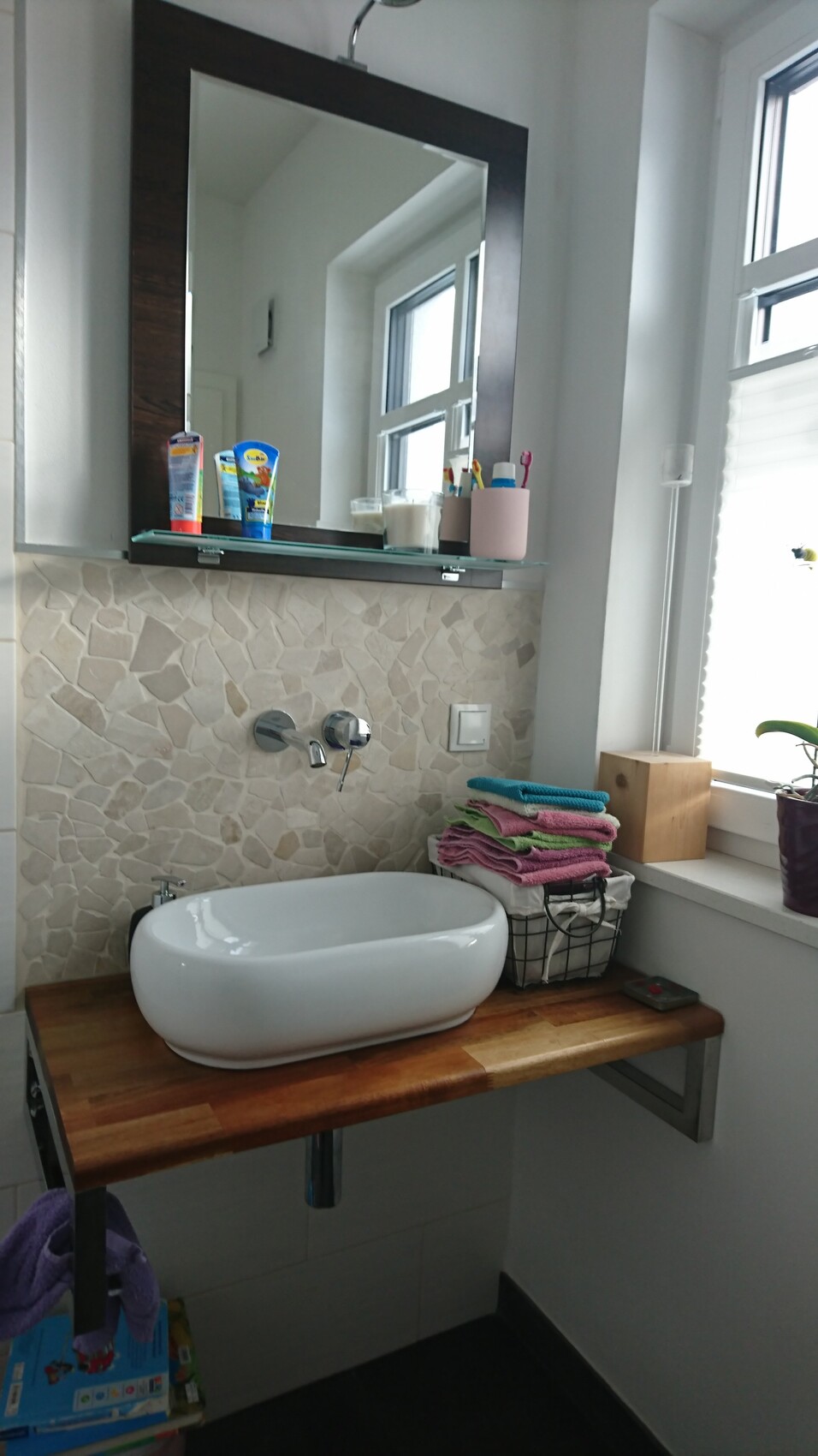 Weißer Vessel-Sink auf Holzablage, Steinwand, großer Spiegel, gestapelte Handtücher.