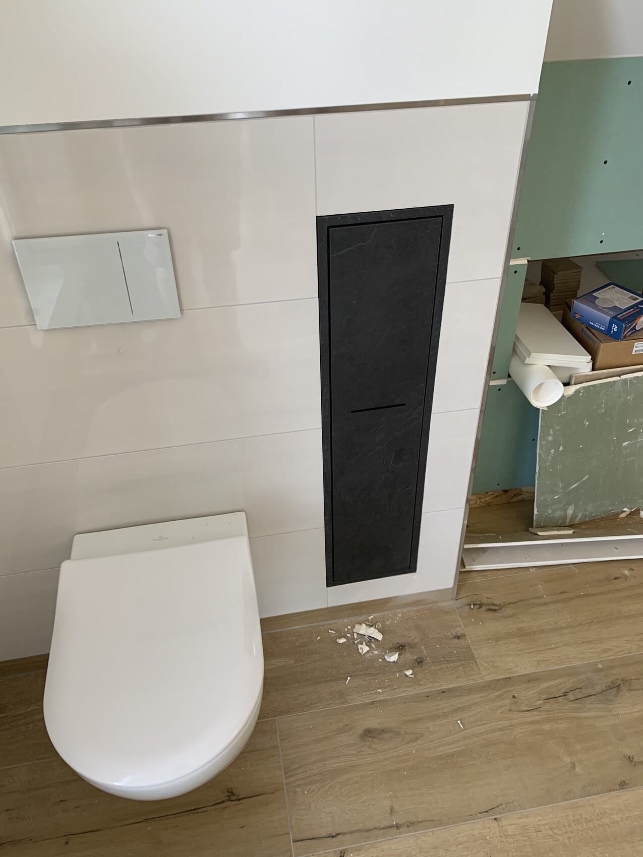 Moderne Toilette mit verdecktem Spülkasten und schwarzer vertikaler Frontplatte, Baubereich rechts.