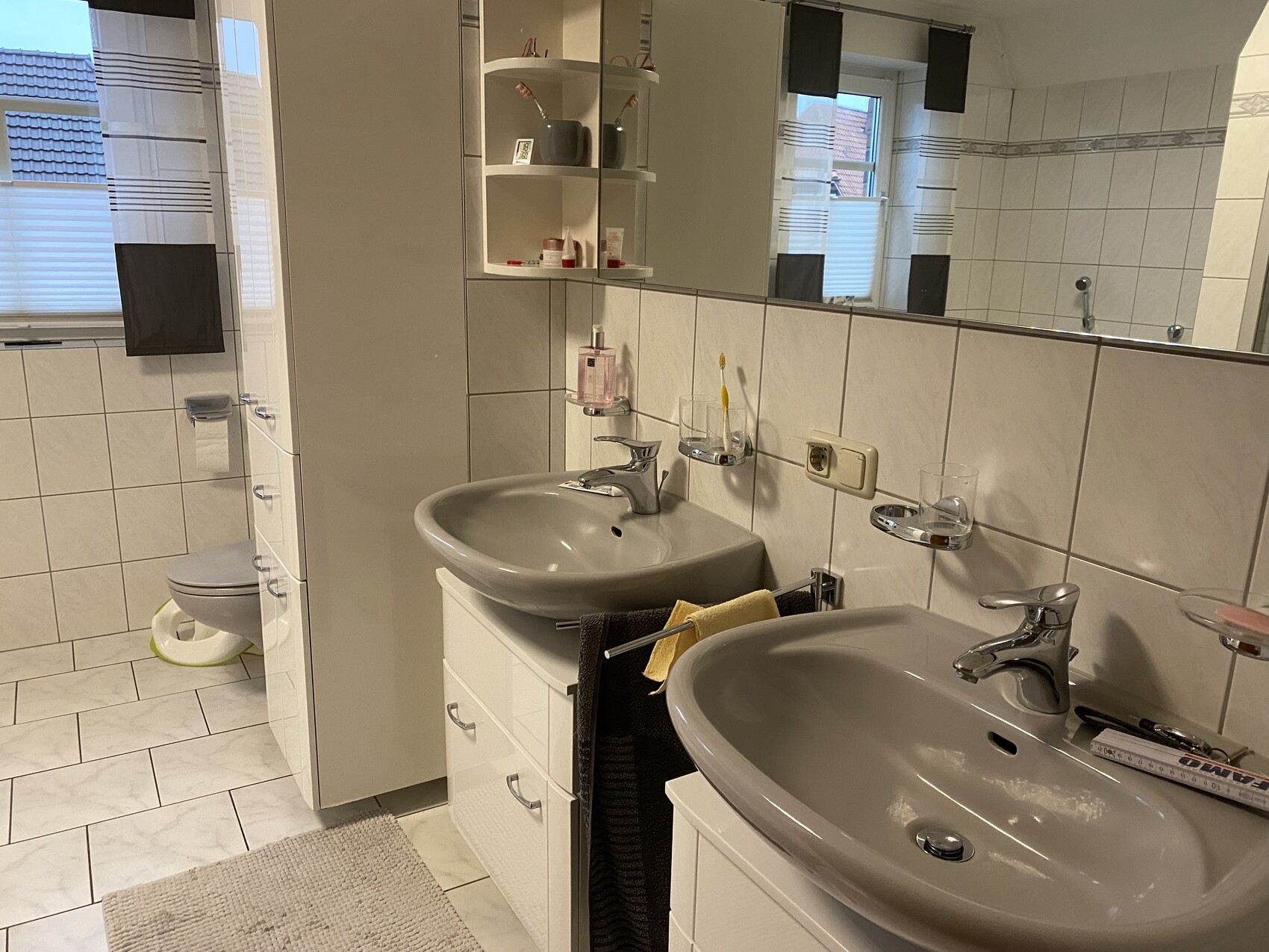 Badezimmer mit zwei Waschbecken, großem Spiegel, WC links und Fliesenboden.