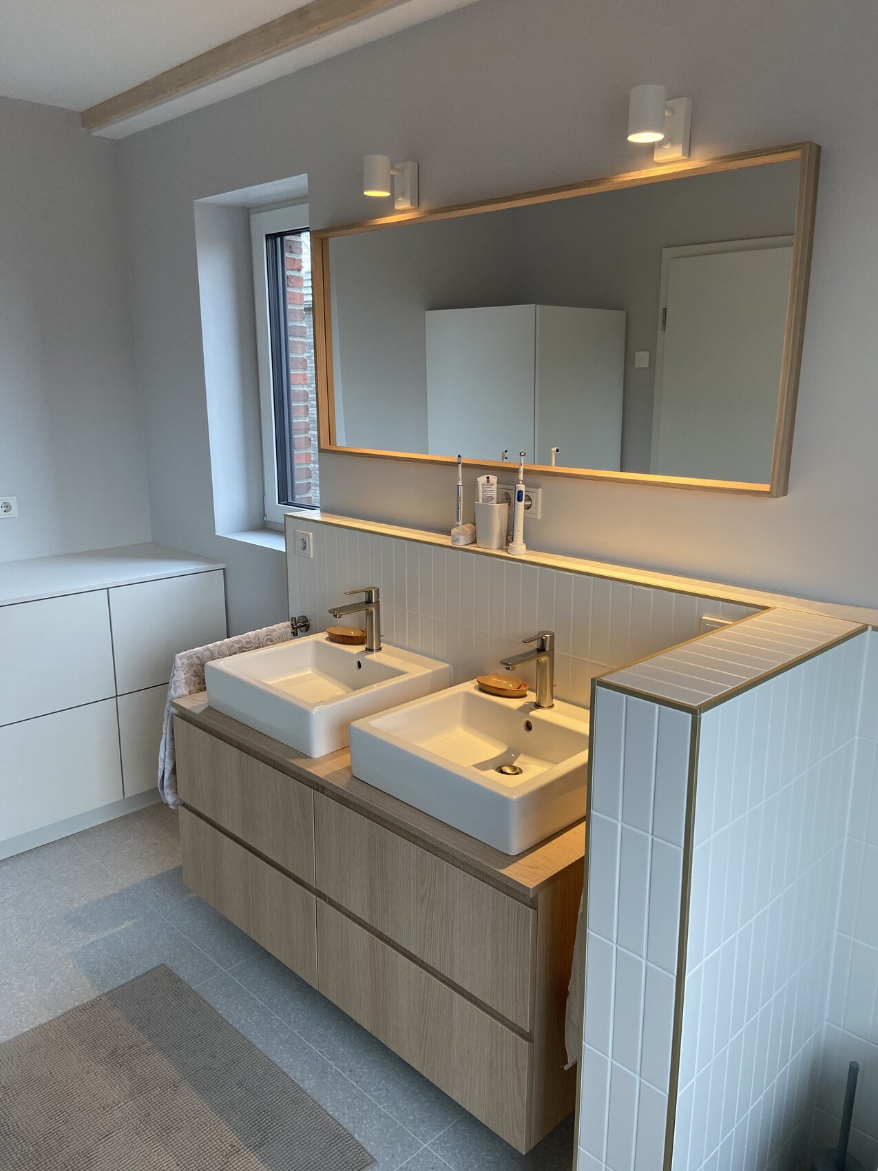 Modernes Badezimmer mit Doppelwaschtisch, zwei Waschbecken, großer Spiegel, Holzunterbau, Fenster.