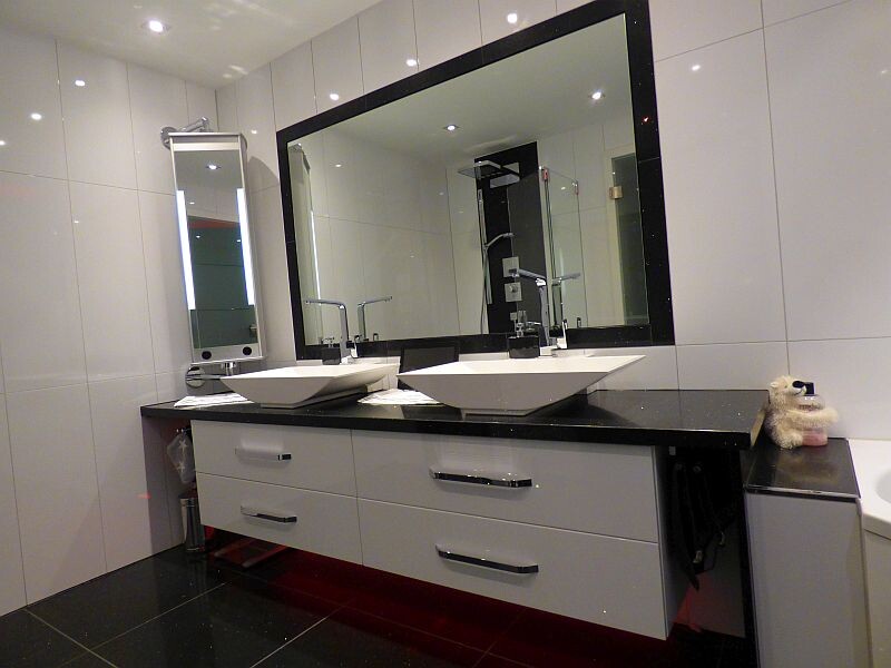 Modernes Badezimmer mit Doppelwaschbecken, großem Spiegel, Glasdusche und dunkler Arbeitsplatte.