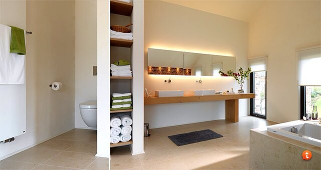 Modernes Badezimmer mit Holz-Waschtisch, beleuchteter Spiegel; Toilette links, Badewanne rechts.
