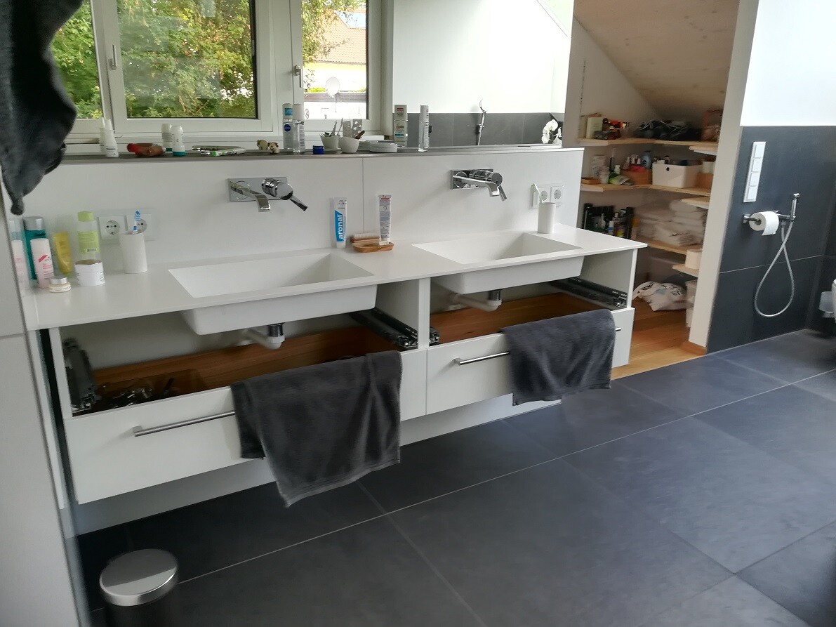 Moderne Doppelwaschbecken mit offenen Schubladen, graue Handtücher, Regal mit Pflegemitteln.