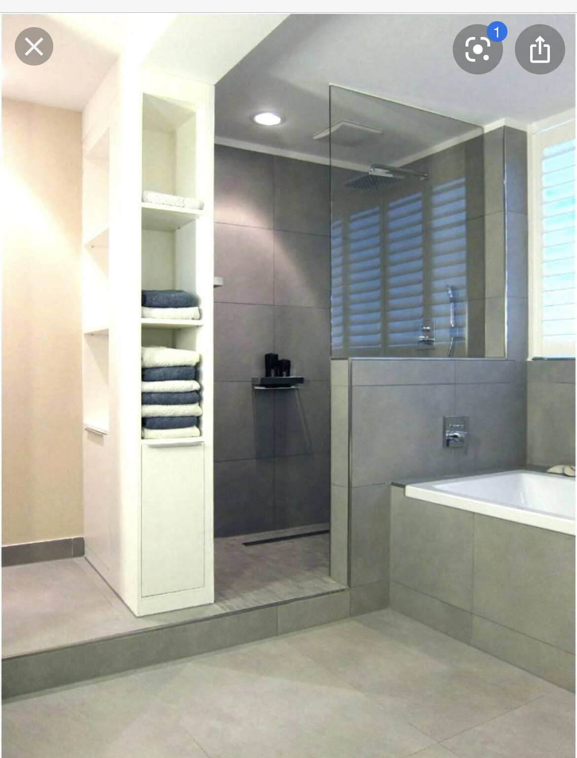 Modernes Badezimmer mit grauen Fliesen, Dusche hinter Glas, Badewanne und Regal mit Handtüchern.