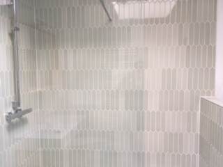 Badezimmer-Duschbereich mit Glasabtrennung und hellgrauen Fliesen