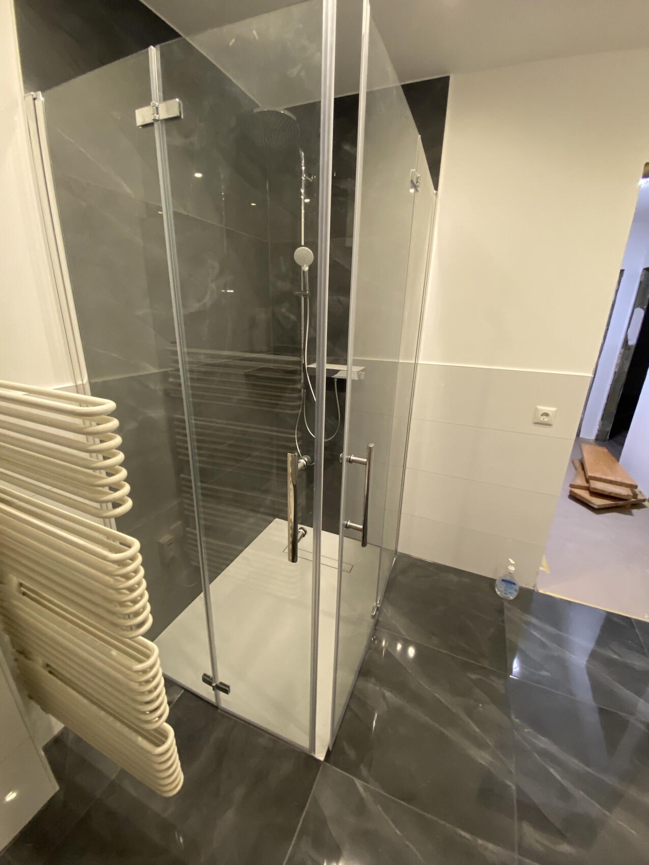 Modernes Badezimmer mit rahmenloser Glasdusche, dunklen Fliesen und Handtuchheizkörper.